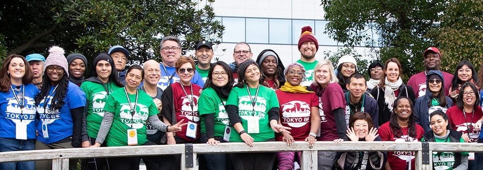 large group of people smiling on a wooden bridge wearing colorful printed shirts